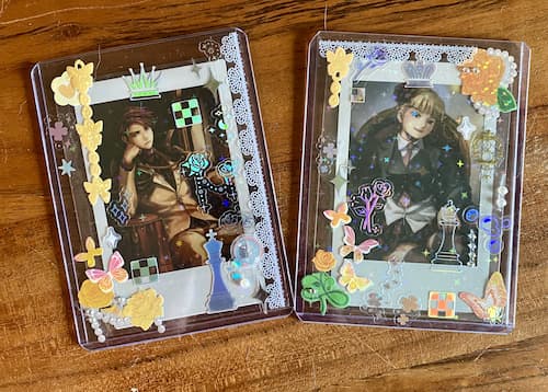 two photocards of beatrice and battler from umineko using
                                                             battler's EP6 portrait and beatrice's EP2 portrait.
                                                             the card holders are decorated in stickers, some of
                                                             which are gold roses, some are chess themed, and
                                                             some are holographic.